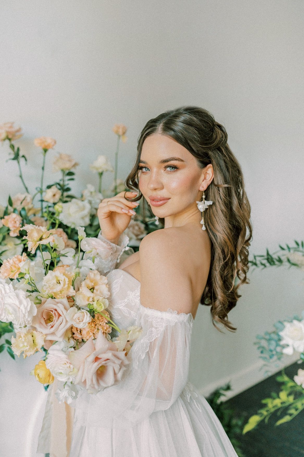 A Calyx Floral Design model standing in front of a mantel arrangement, smiling, as she holds her peach and blush bouquet