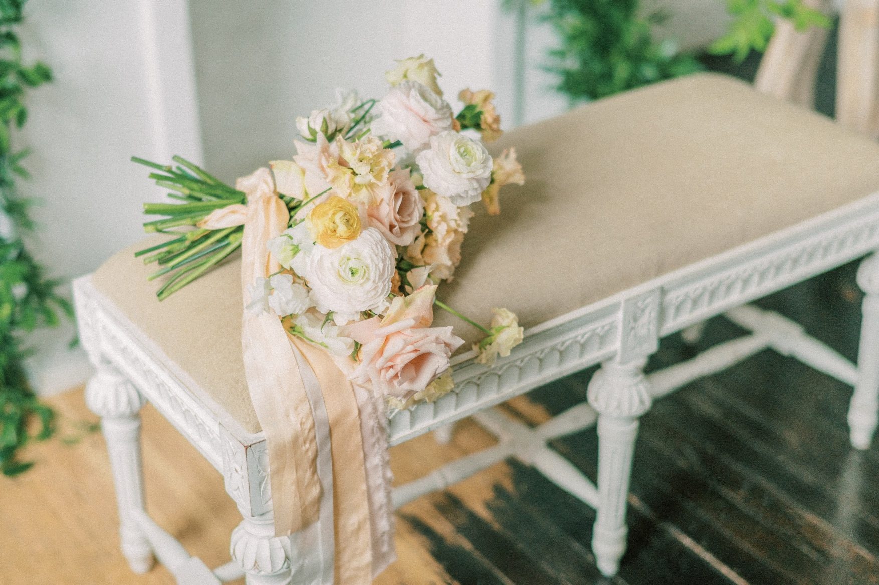 A Calyx Floral Design bridal bouquet in peach, blush and white sitting on a bench with silk stem wrap draping over the side