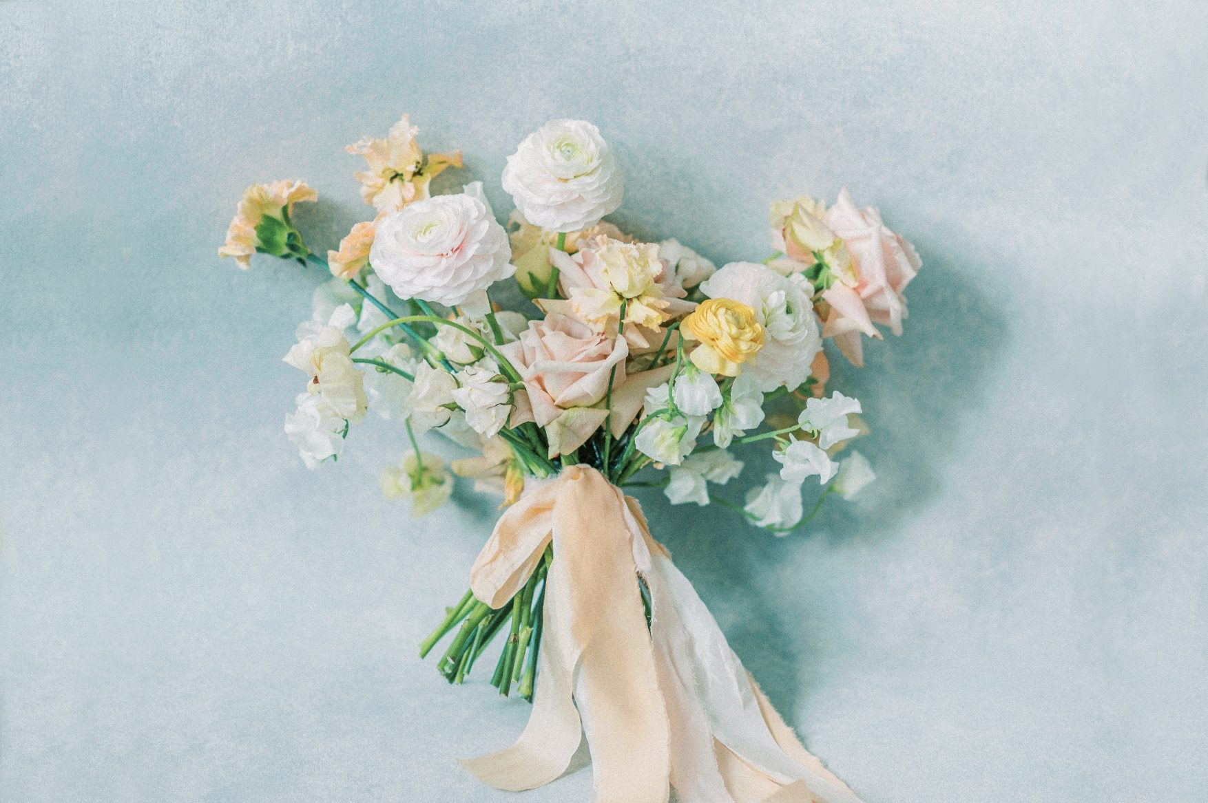 A flat lay shot of a Calyx Floral Design Bridal bouquet in peach, pink and white with beautiful silk stem wrap