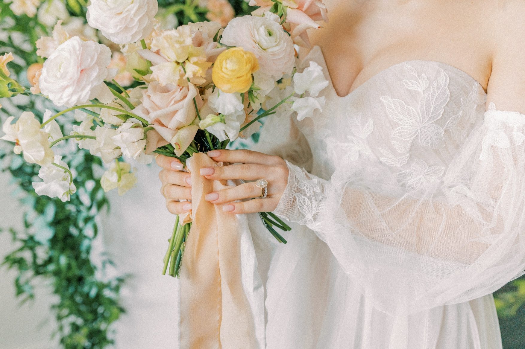 A close up of our model holding a peach and blush Calyx Floral Design bouquet, with silk stem wrap trailing down