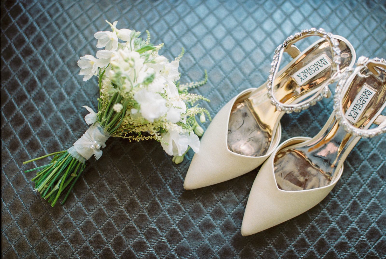 A flat lay image of a white posy bouquet with delicate silk stem wrap and the bride's designer shoes