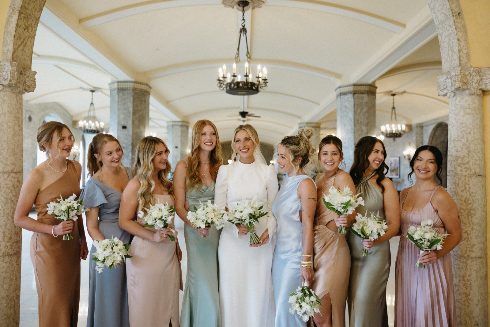 A Calyx bride and her bridesmaids wearing muted pastels all holding white posy bouquets