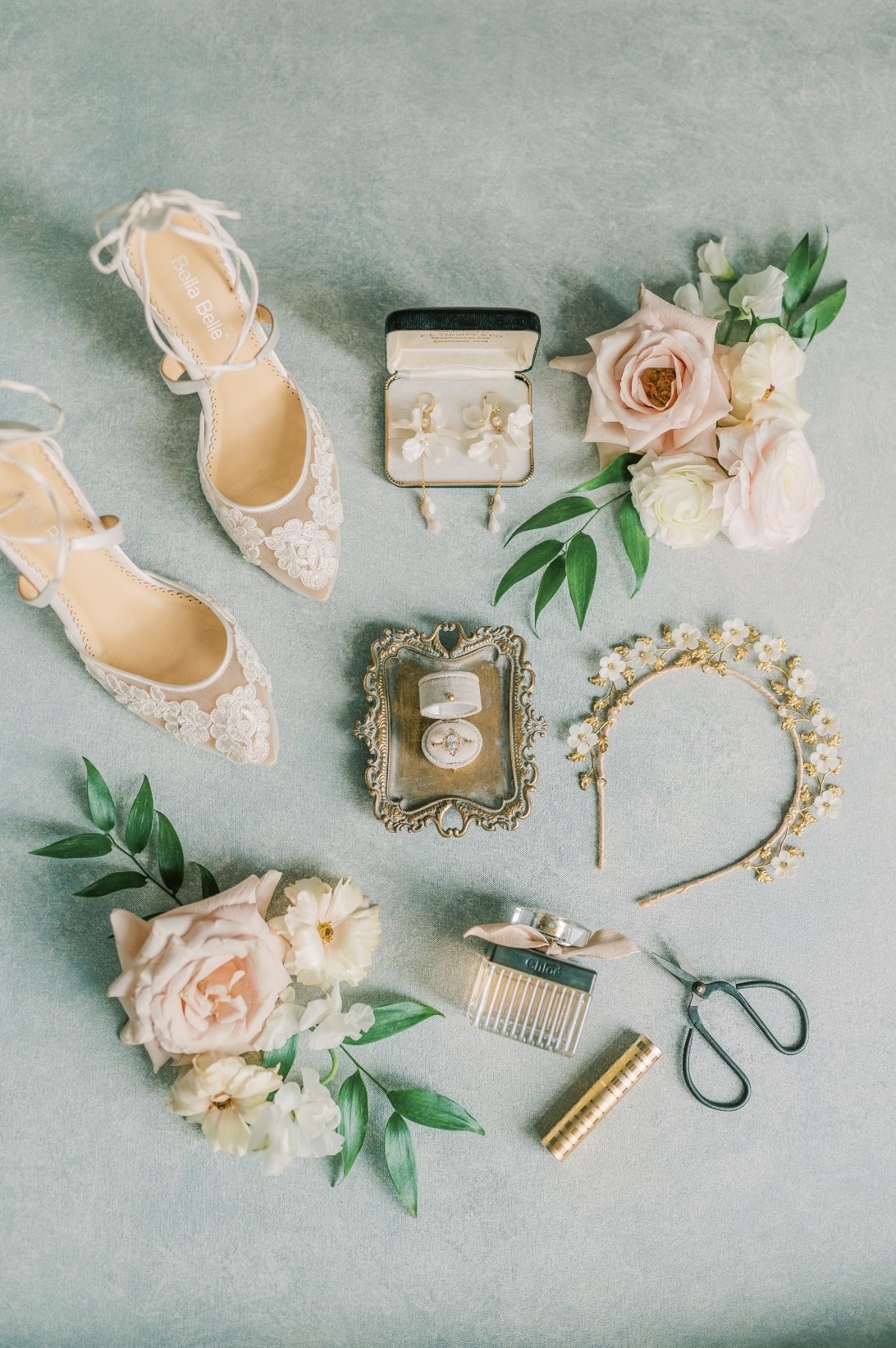 A flat lay shot of bridal accessories - Bella Belle shoes, wedding ring, perfume, headband, earings and flowers