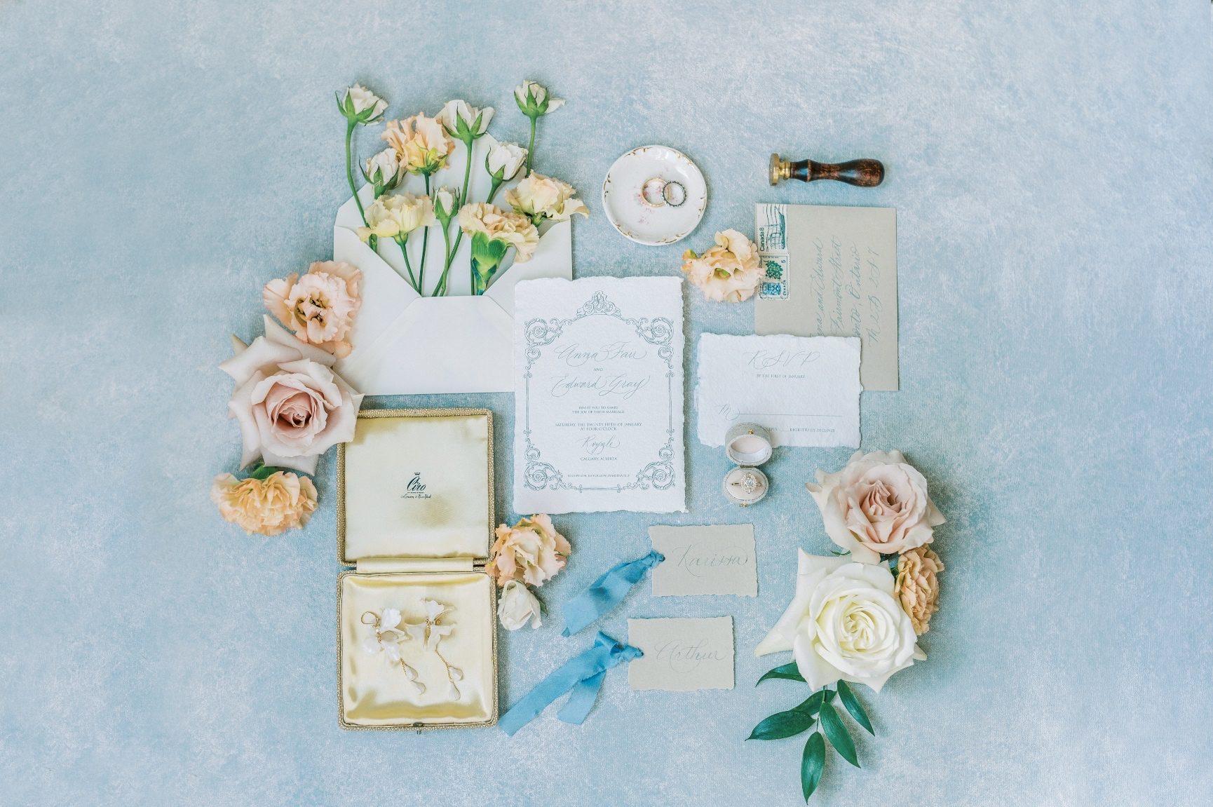 A flat lay shot of the beautiful stationary - wedding invitation, place rsvp cards, place card accented by pretty peach, blush and white blooms