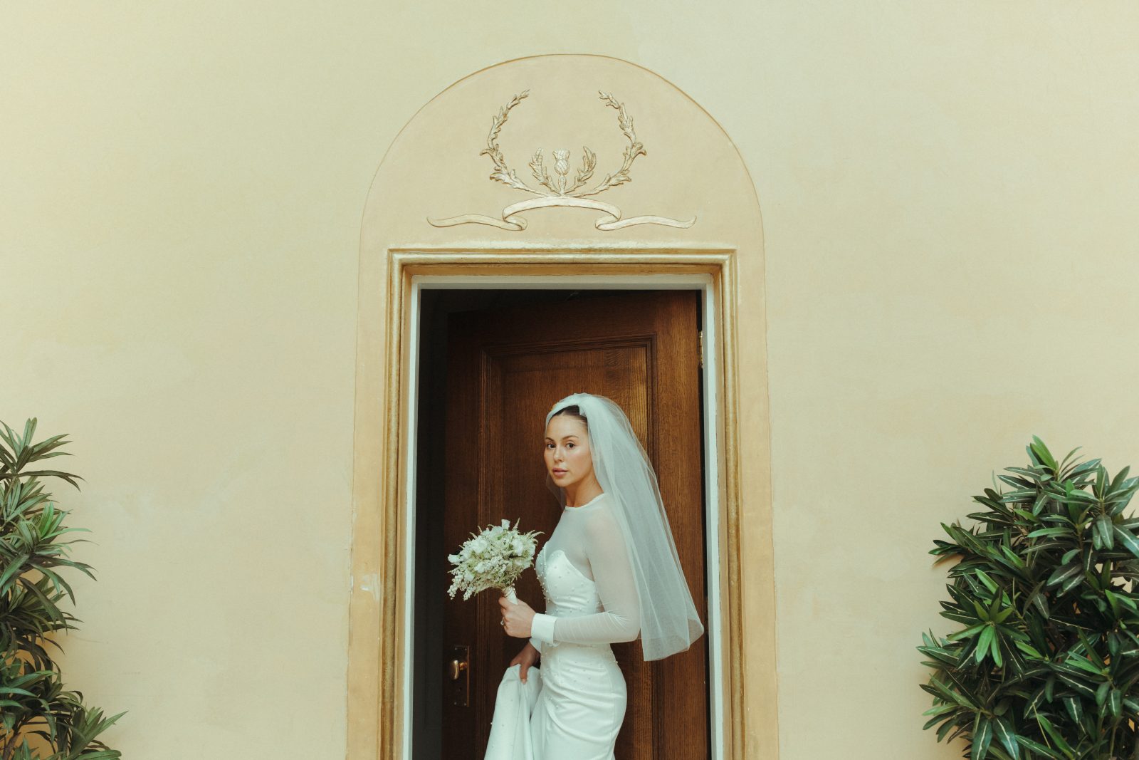 A glamorous Calyx bride holding a white posy bouquet entering a door at the Banff Fairmont