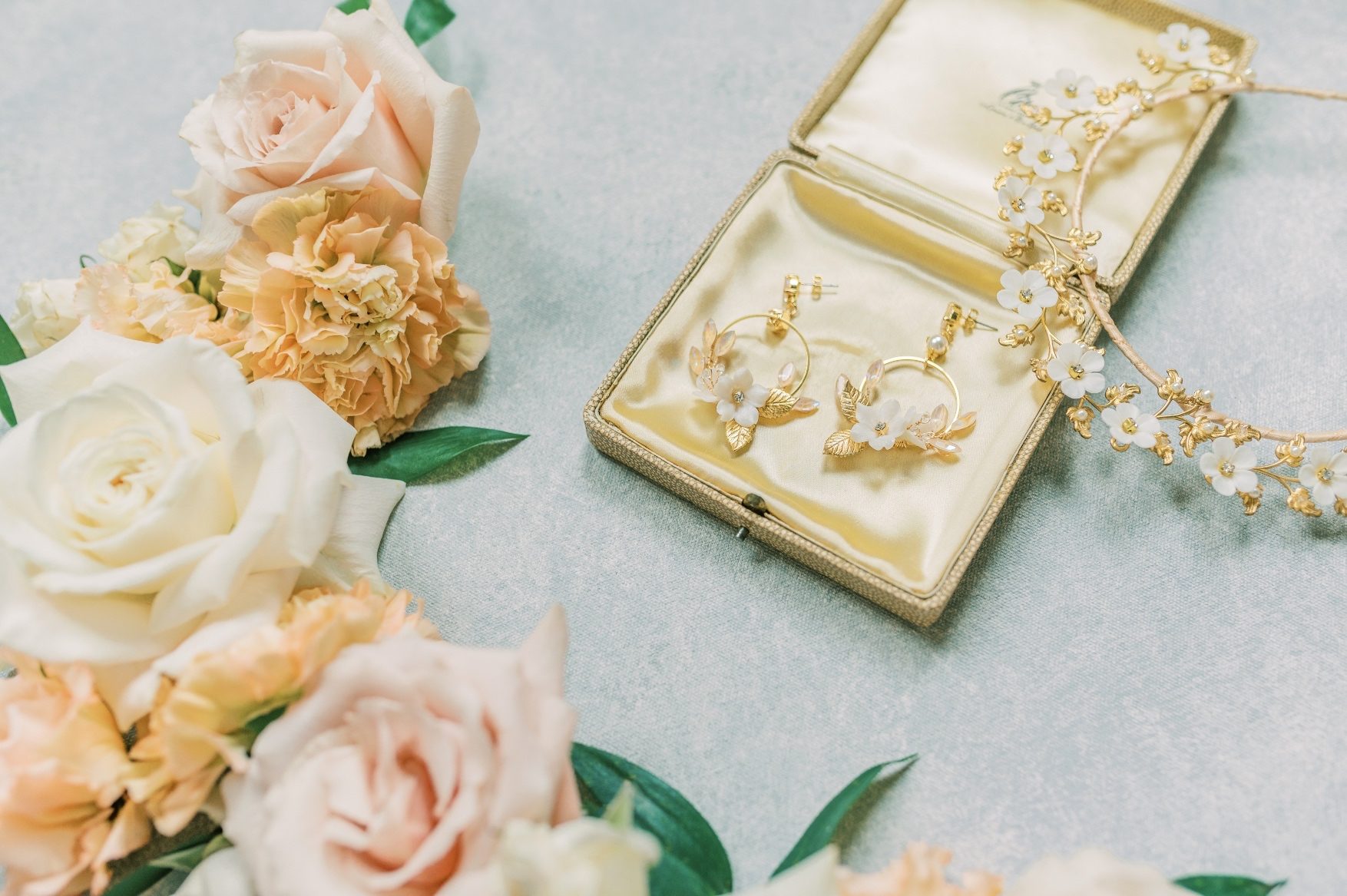 A close up of the earings in a decorative jewelry box with a mixture of peach and blush blooms nearby