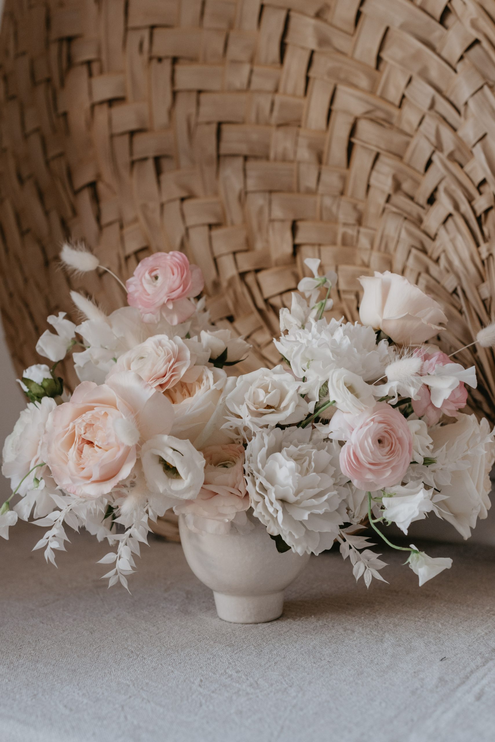 A beautiful front facing asymmetrical floral arrangement with a mixture of pastel tones in a white pedestal vase.