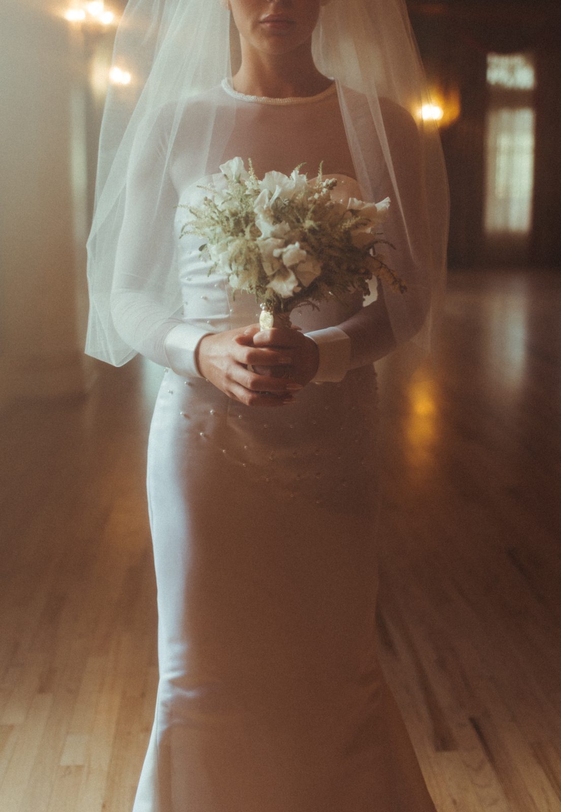 A close up shot of a Calyx bride's beautiful gown as she holds up her white posy bouquet