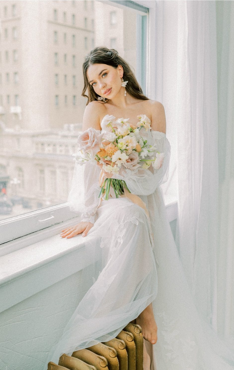 A Calyx Floral Design model sits on a window sill holding on to her peach and blush bouquet