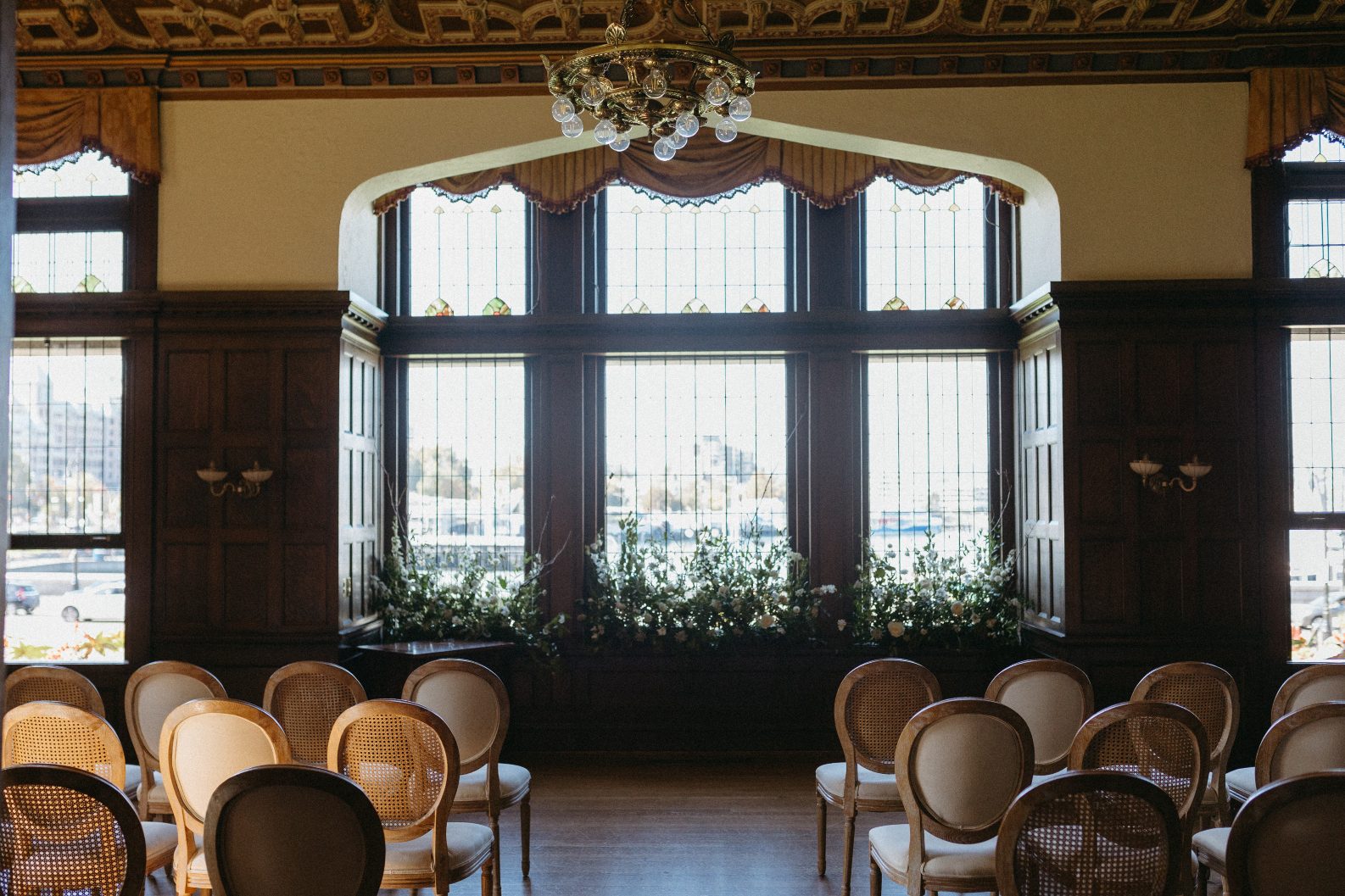 A view of the ceremony location, the library of the Fairmont Empress in Victoria. Large windows as the backdrop, with large white and green arrangements at the base.