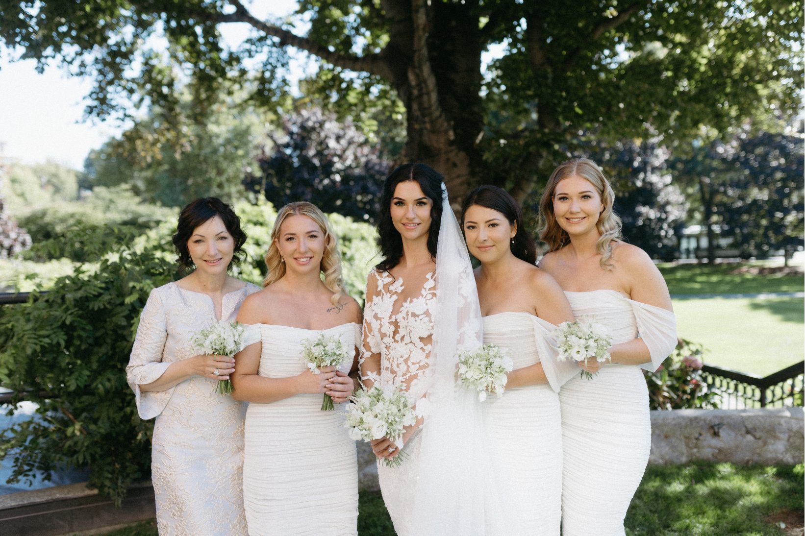 Stephanie and her bridesmaids all stand in the gardens wearing white, and holding white posy bouquets