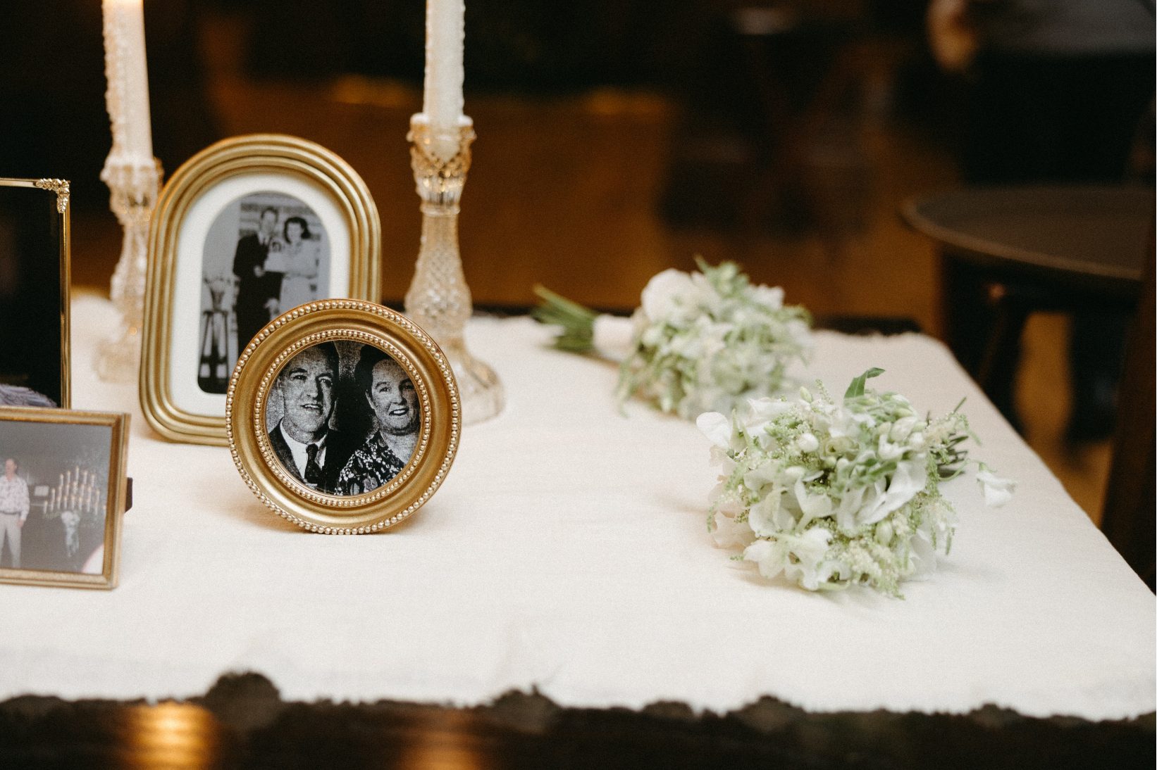 A detail shot of the reception, featuring black and white photographs of the couples grandparents in decorative frames with white posy bouquets laying nearby.