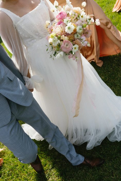 A Calyx Floral Design bride walking down the aisle carrying a bouquet of white, pink and peach including some locally grown flowers