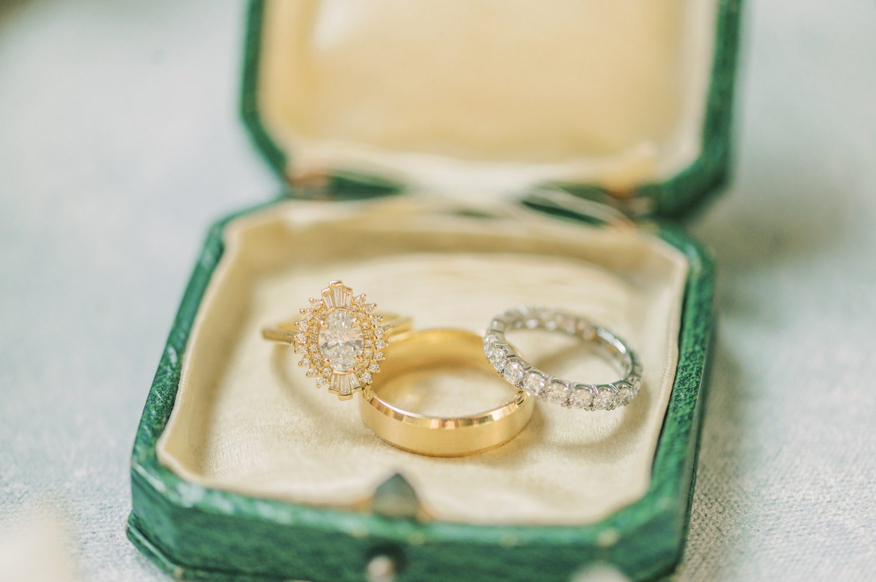 A close up of the wedding ring and wedding bands in a green decorative jewelry box