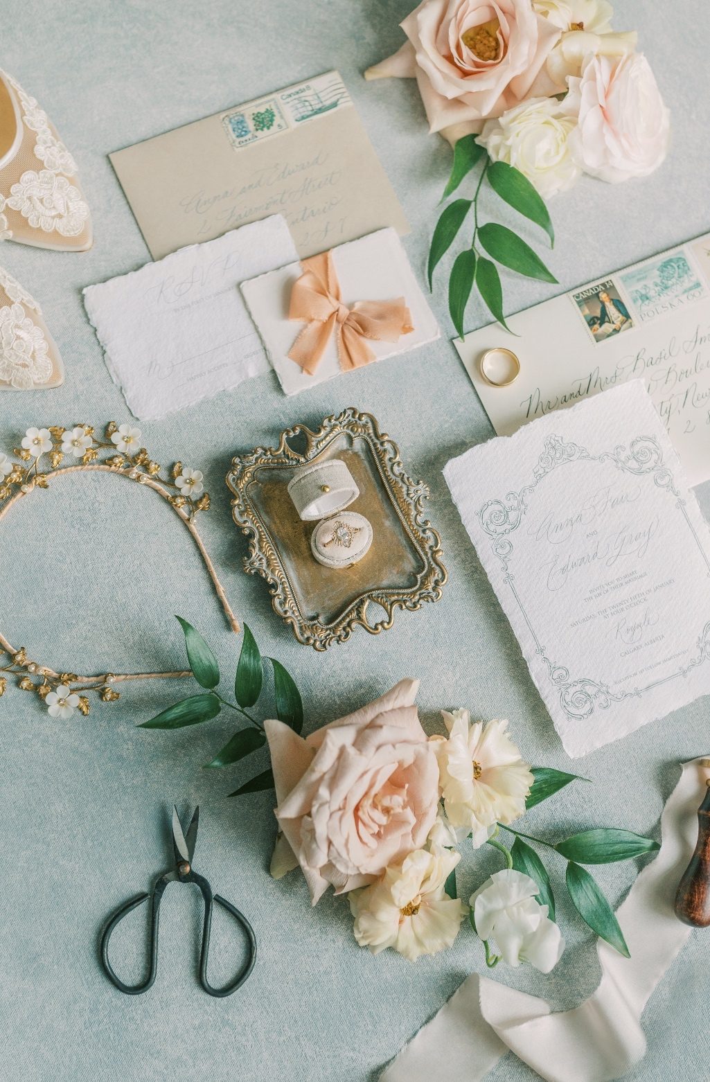 A pretty flat lay shot of assorted details - the wedding invitation, wedding ring on a decorative tray, bridal headband accented by pretty floral clusters