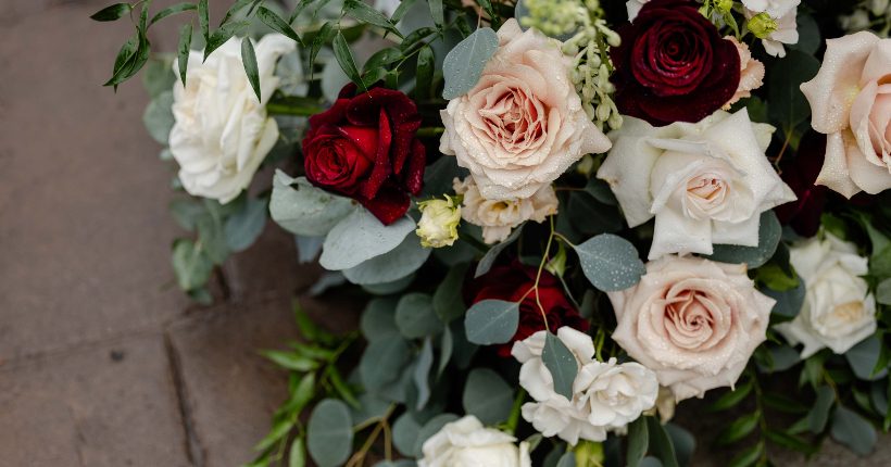 A close up of the aisle arrangements in burgandy and ivory with roses, spray roses, lisianthus eucalyptus and italian ruscus.