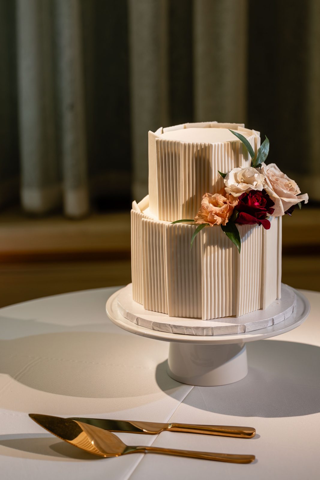 A simple two tier cake with verticle striped texture and a cluster of roses, lisianthus and greenery tucks