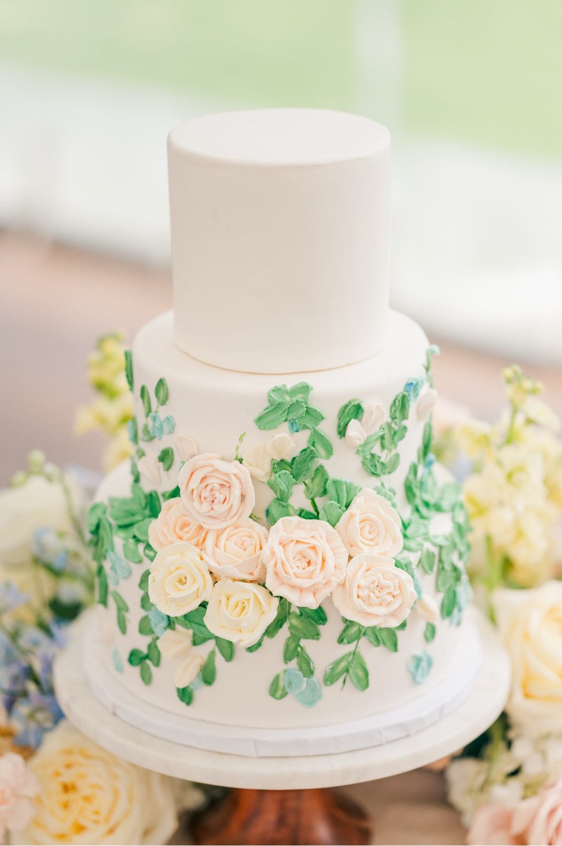 A three tiered cake decorated with green buttercream leaves and ivory icing roses.