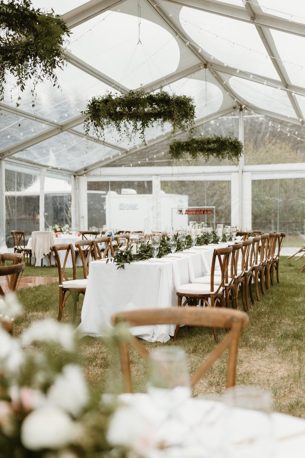 Chandeliers Inside of a reception tent, large floral chandeliers hang from the ceiling over long rectangular tables with a long garland as a centrepiece.
