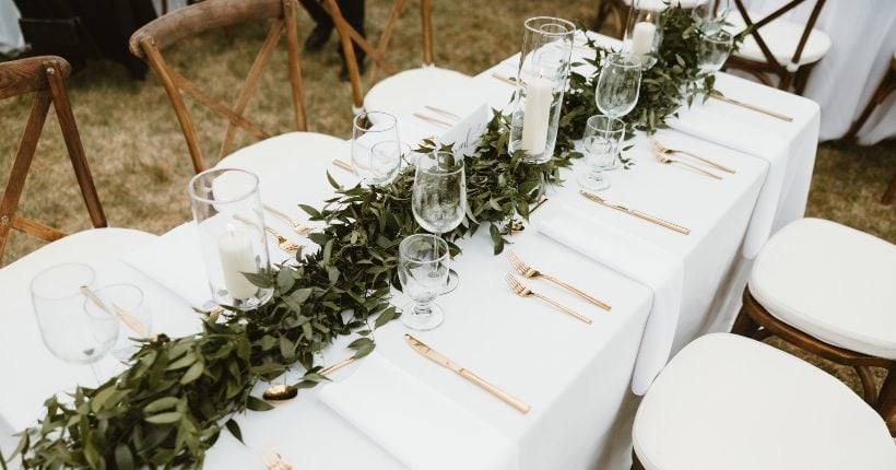 Garland A lush garland draped down the center of a long table with white linens, pillar candles and elegant wooden chairs.