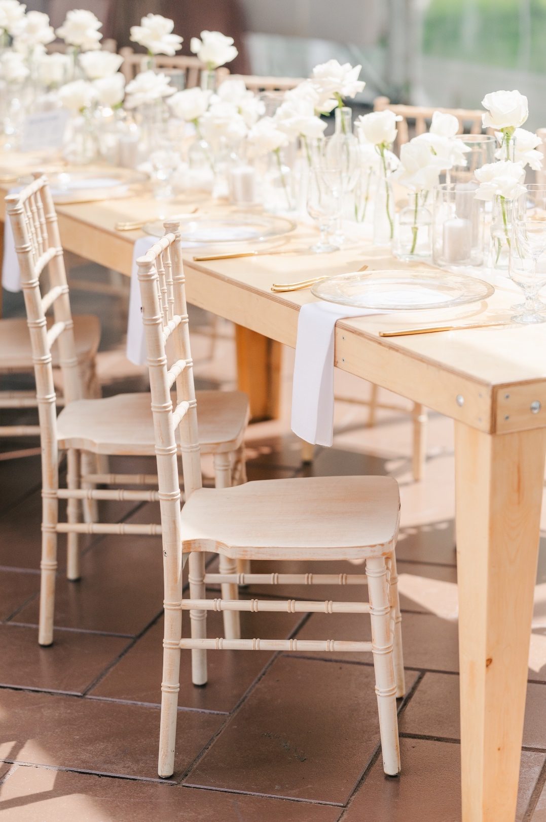 A long table with various bud vases with white roses running the length of the table