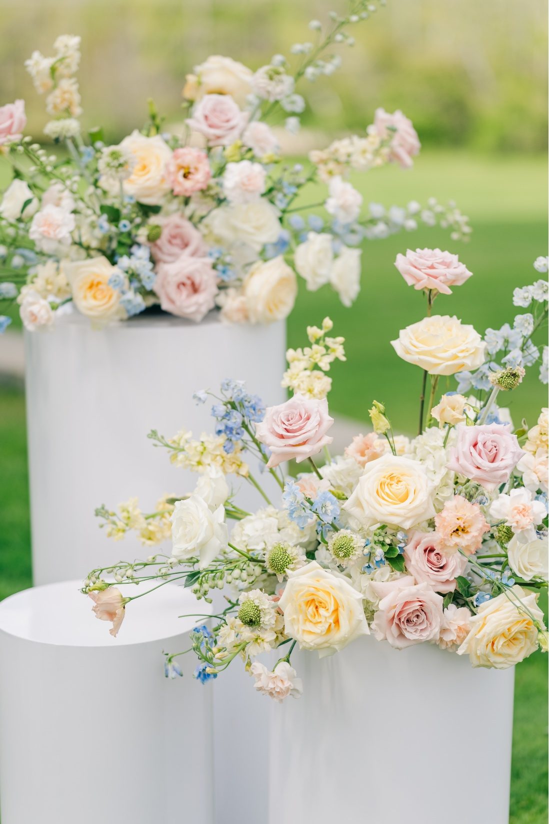 Big, beautiful pastel arrangements sitting on top of white cylinder pillars at the end of the aisle.