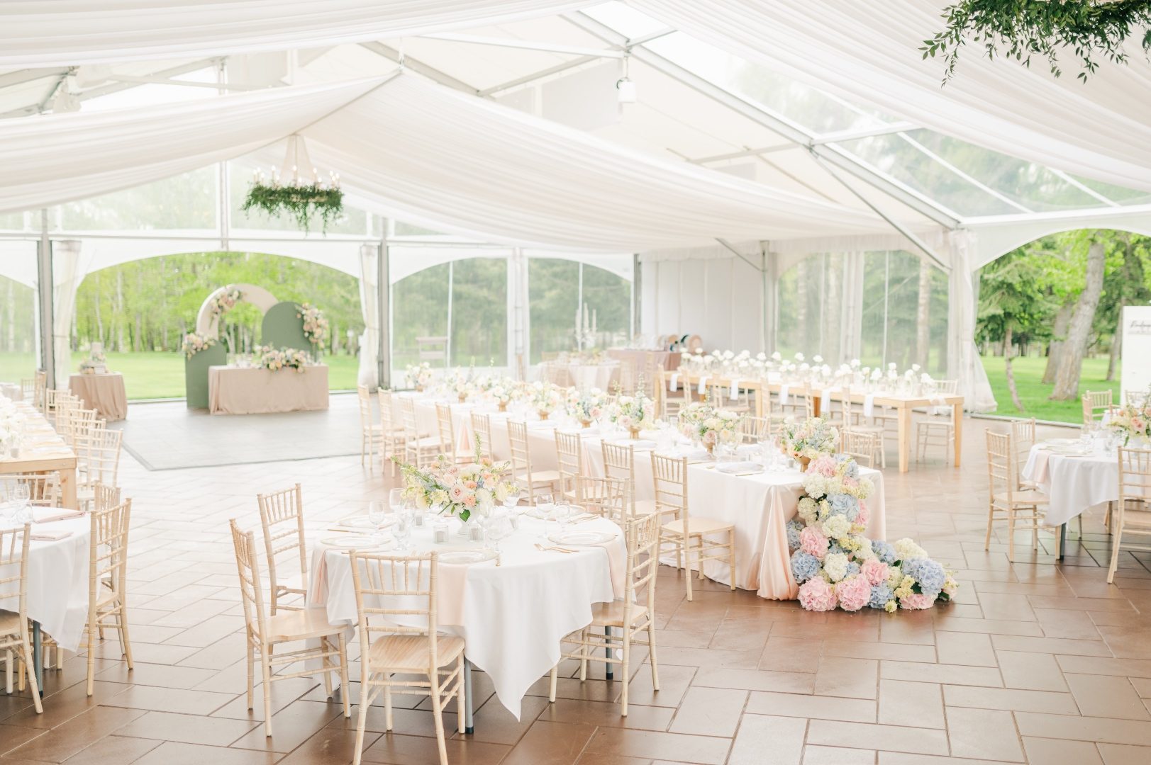 A view of inside the tent at Hilltops Open House, featuring a combination of round tables, long tables and a sweetheart table with a backdrop.