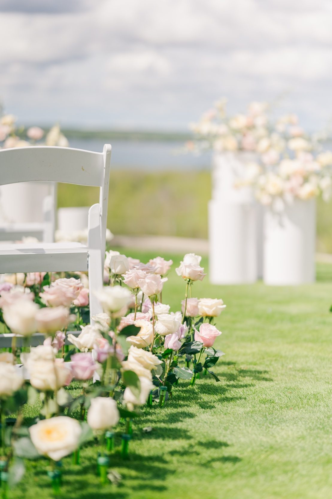 A view of the pastel roses lining the aisle, with the arrangements on large white pillars in the background