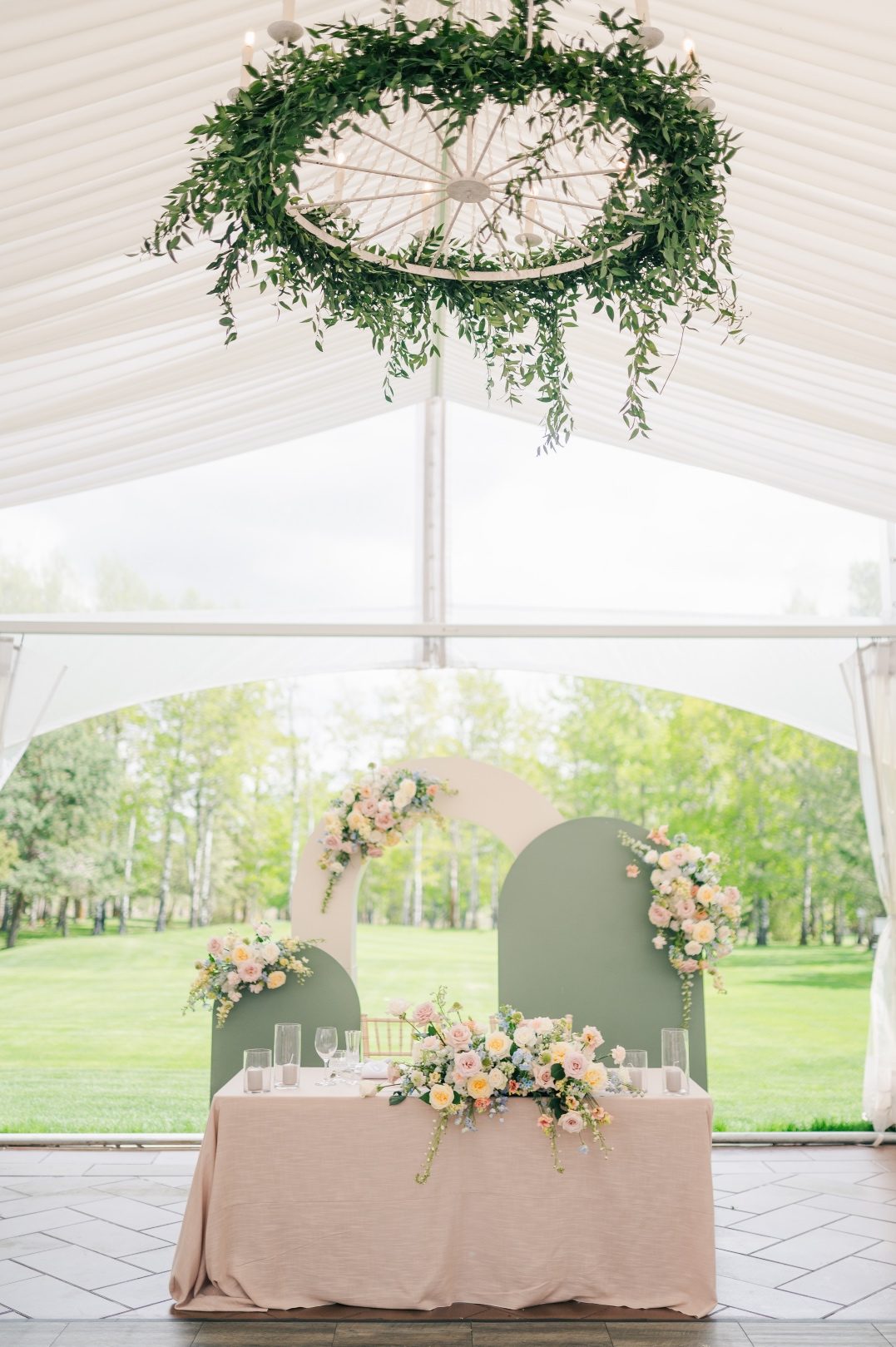 A photo showcasing the beautiful sweetheart table with the mod backdrop as well as a gorgeous chandelier with lush green Italian ruscus draping down.