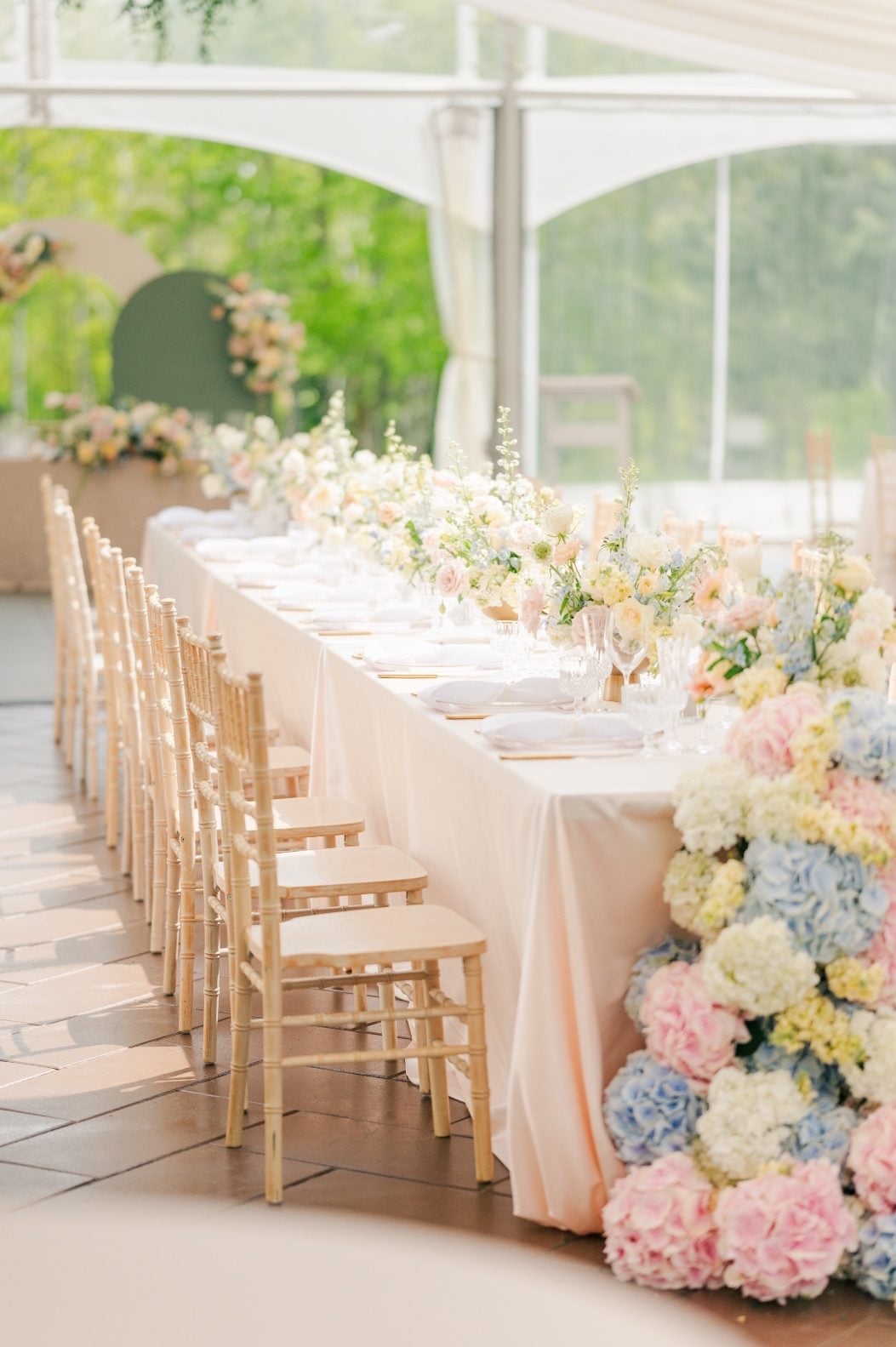 A long table with chiavari chairs, pastel compote centrepieces and a waterfall of hydrangea blooms cascading down the front