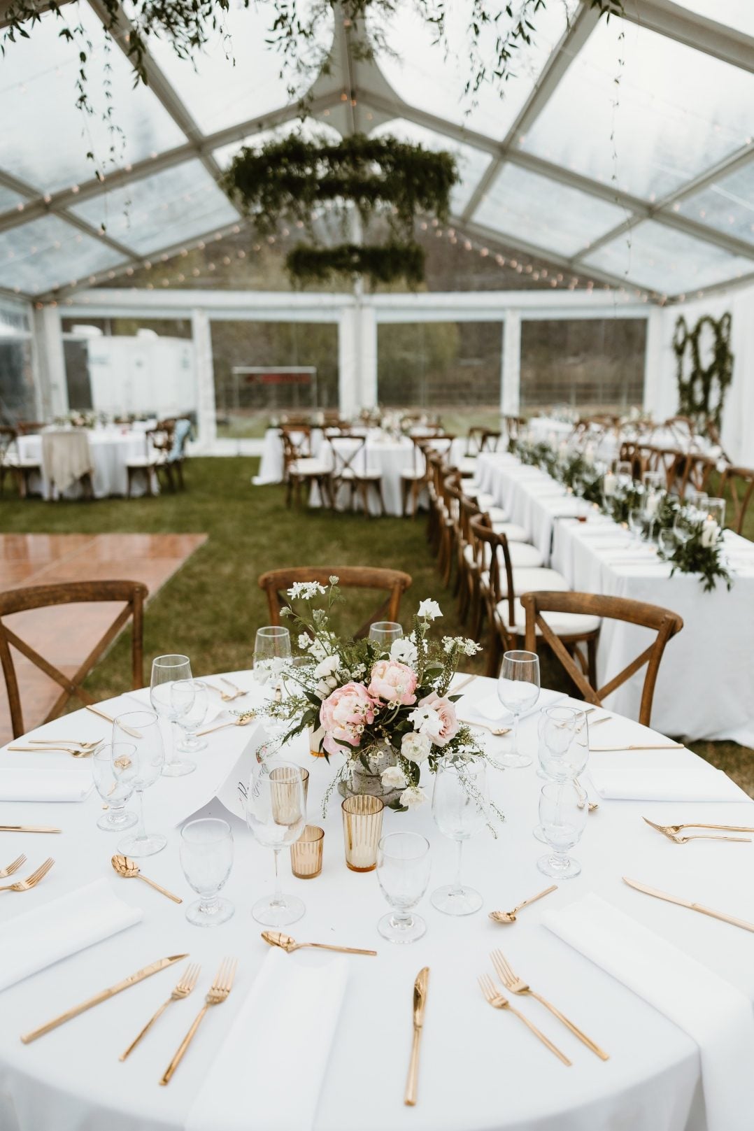 Tent Reception The overall set up of the reception tent, with greenery chandeliers, long tables with garland, round tables with centrepieces and hoop wall accents.