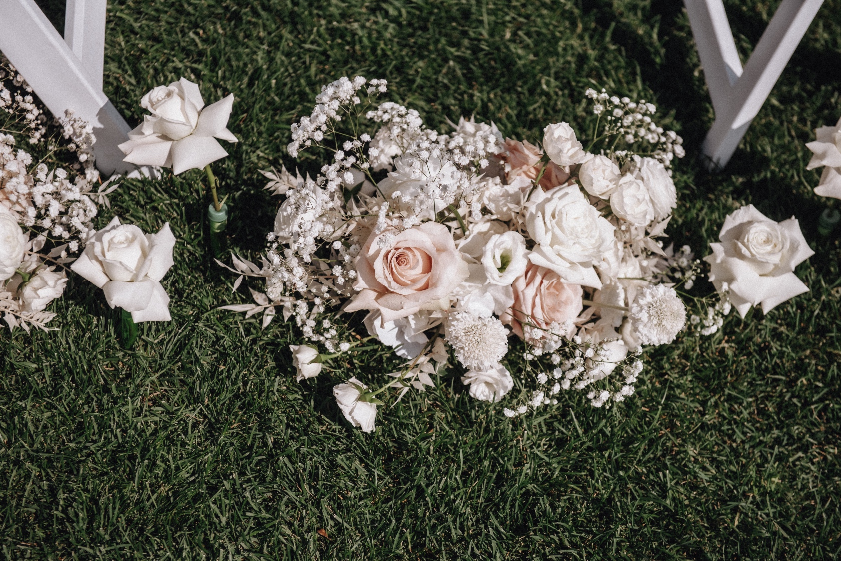 Aisle Arrangements A picture of the aisle arrangements from above showing beautiful roses, ranunculus, scabiosa, baby's breath and bleached ruscus as well as a couple of the roses standing up out of the ground from their water picks.