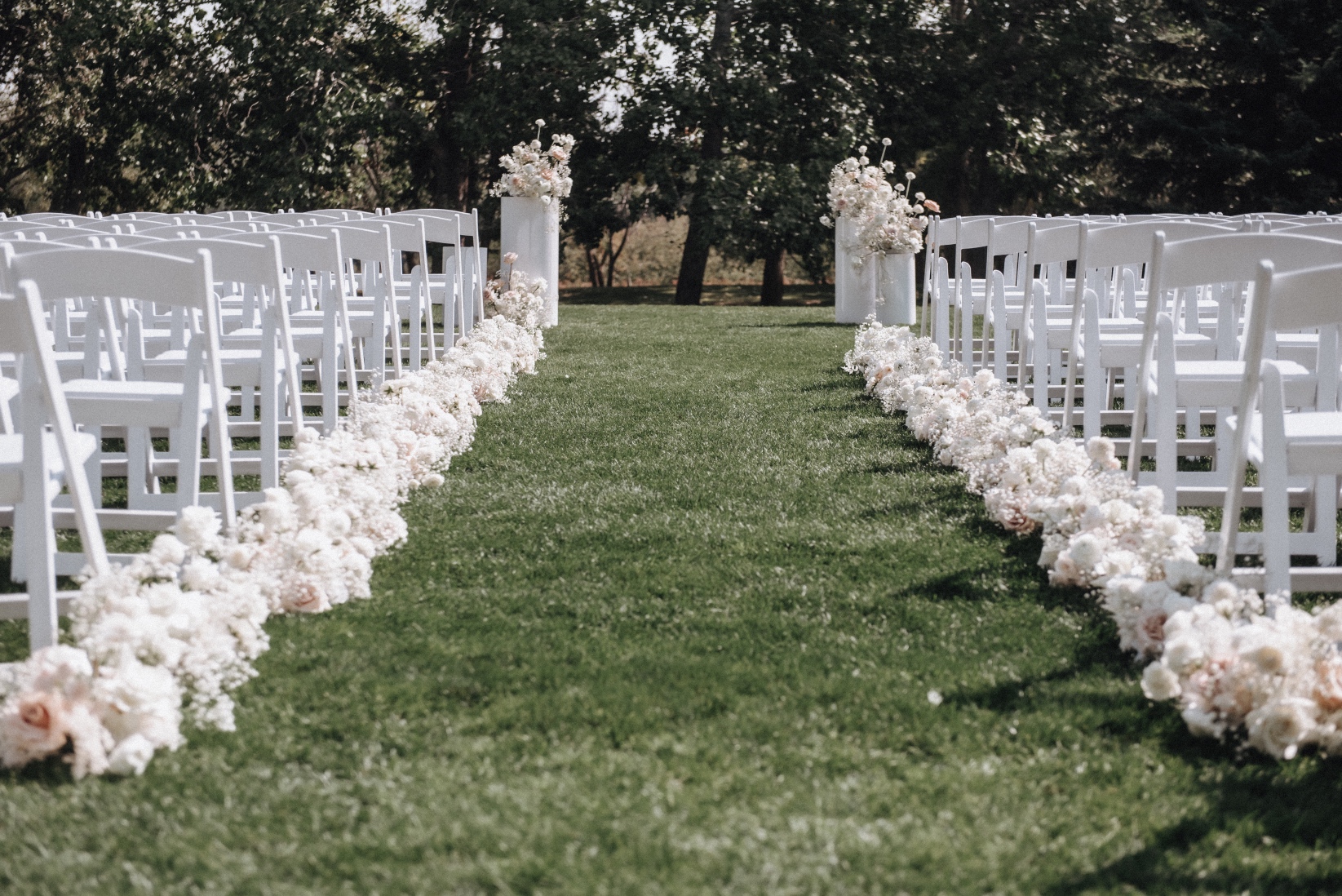 Aisle The ceremony set up at Hilltop Wedding Center, beautiful natural scene with rows of white chairs and rows of white arrangements lining the aisle.