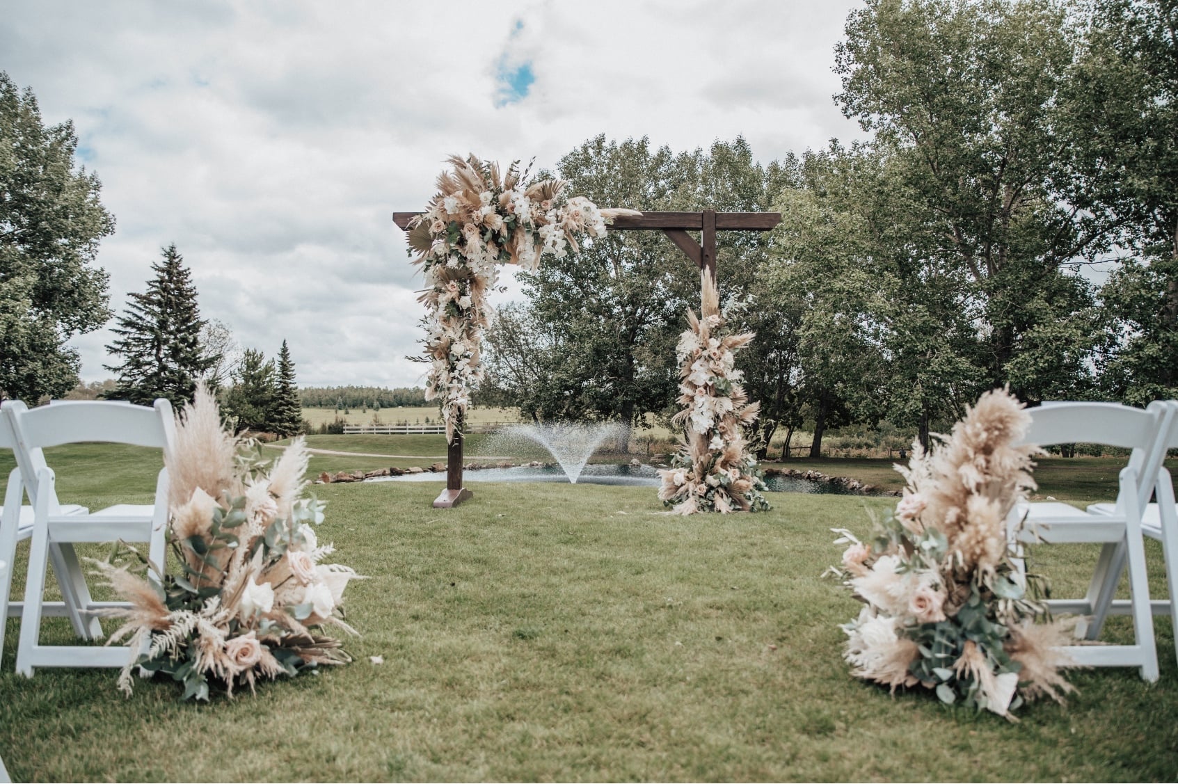 The end of the aisle with two stunning aisle arrangements and big, beautiful archway with the fountain of the pond in the distance.