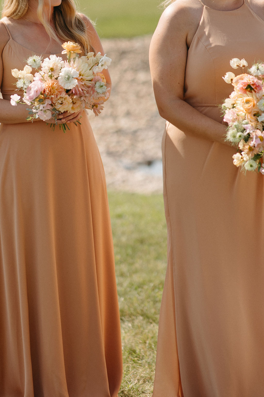 The bridesmaids in their satin peach gowns holding peach, pink and white bouquets.