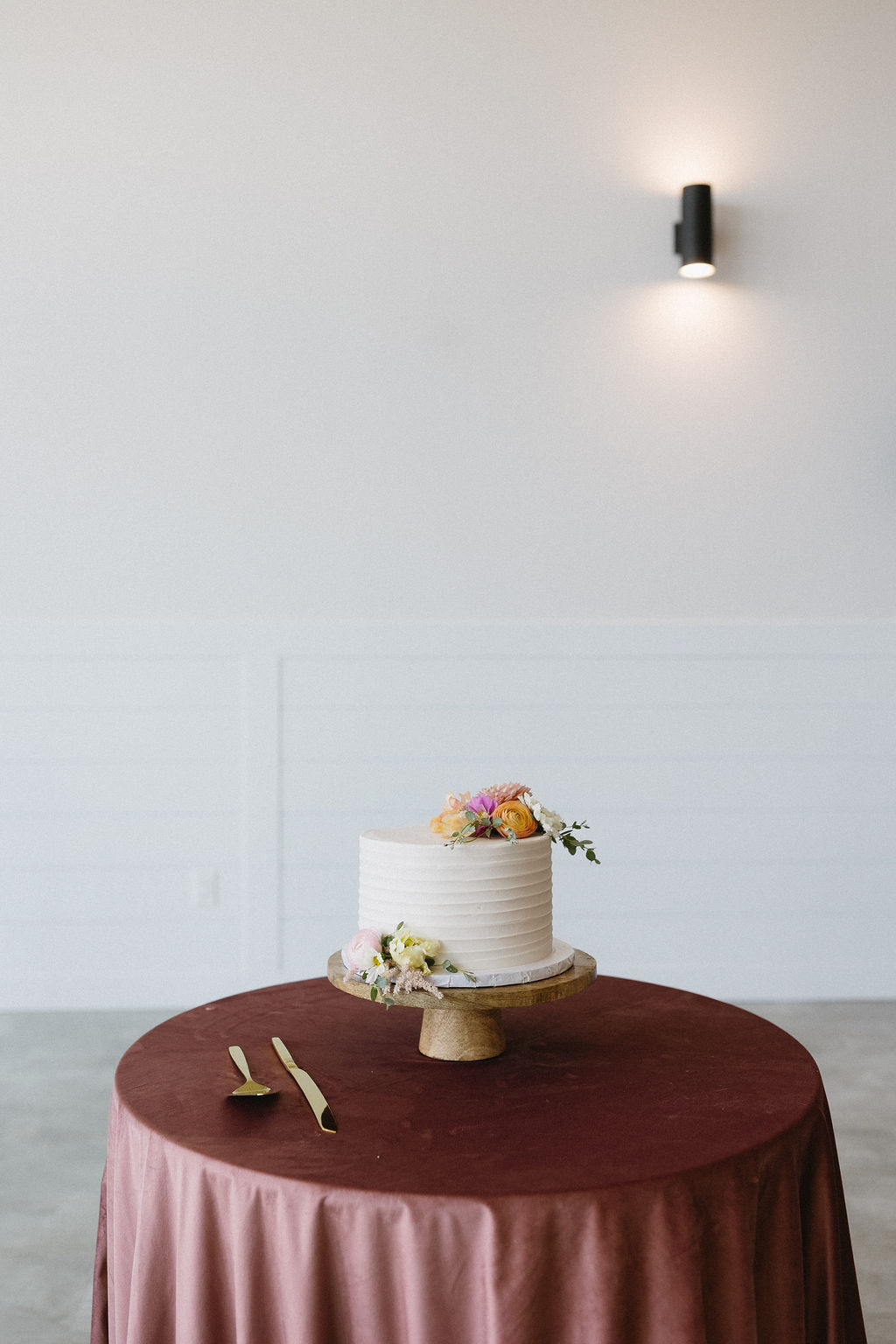A simple cake adorned with pink and peach blooms on top of a beautiful wood stand on a satin covered table.