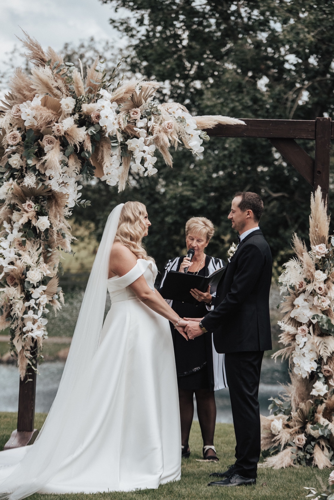 Holly + Scott standing in front of the archway, clasping hands during the ceremony