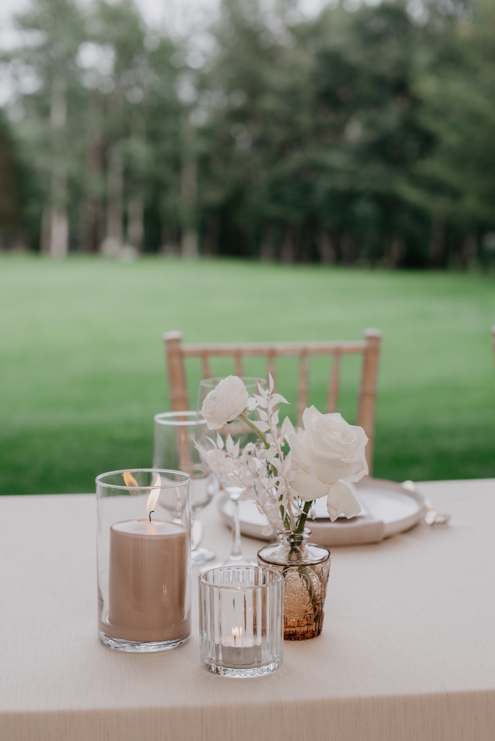 Head Table The head table had pale table cloth, with clustered vases at different heights. light brown bud vases with white blooms, short votive candles and cylindrical vases with nude toned pillar candles