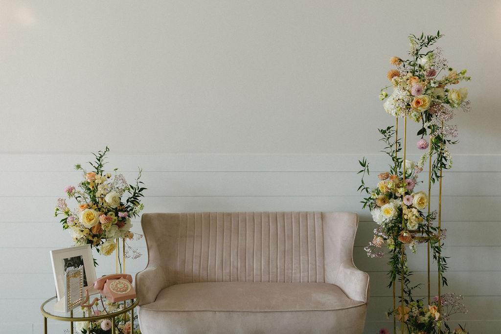A posh little seating area set up at the reception with a blush couch, framed by the beautiful floral stands from the ceremony.