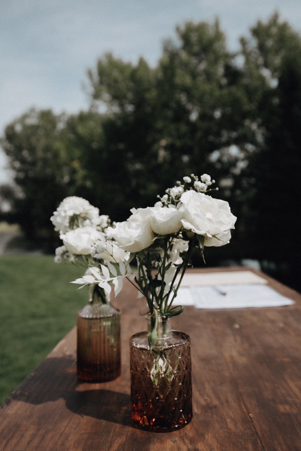 Signing Table A pair of bud vase arrangements in light brown glass with clusters of white blooms sitting on top of the signing table.
