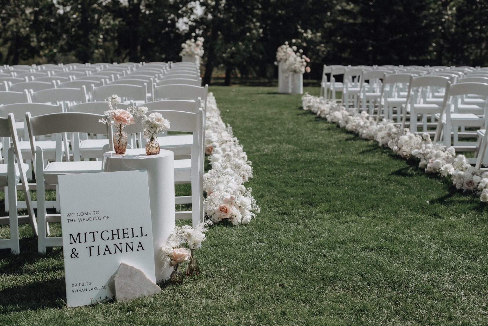 Welcome Sign The start of the aisle showing a welcome sign for the guests, a white pillar and a cluster of bud vase arrangements on top and down on the ground.