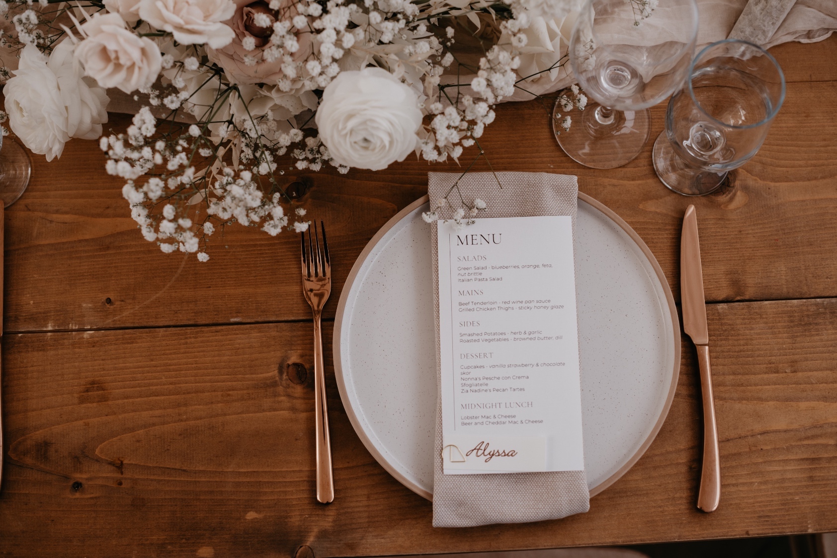 Wood Table A shot looking directly down at a plate showing the simplistic place, linen napkin, elegant menu, copper toned cutlery and a portion of the centrepiece at the top of the image.