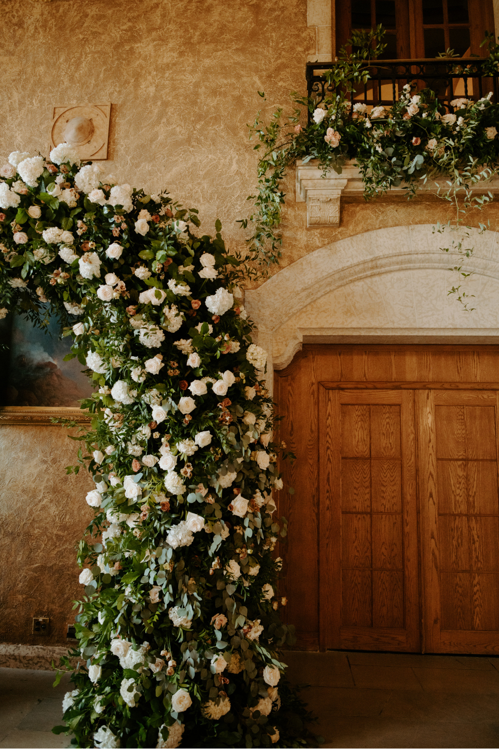 The big, fluffy floral arch, with an arrangement of greenery and roses overflowing from the balcony above it.