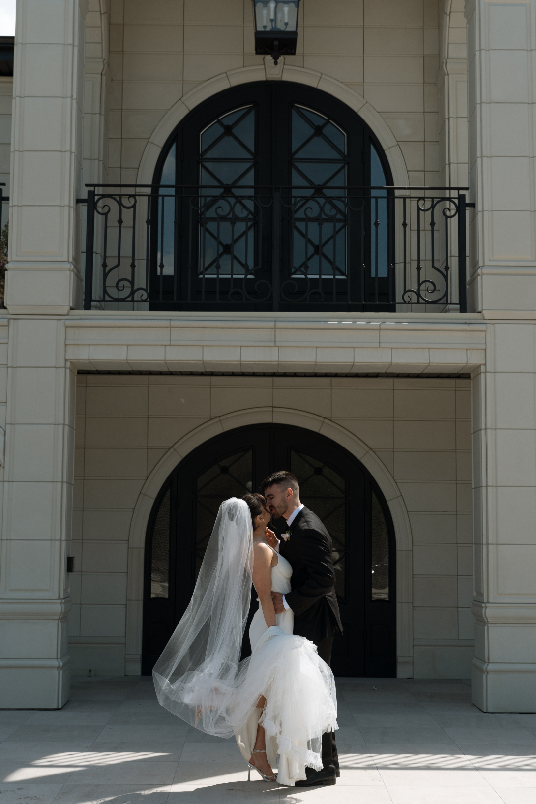 The couple kissing in front of the entrance at Archway Manor, showcasing some of the beautiful detail of the exterior.