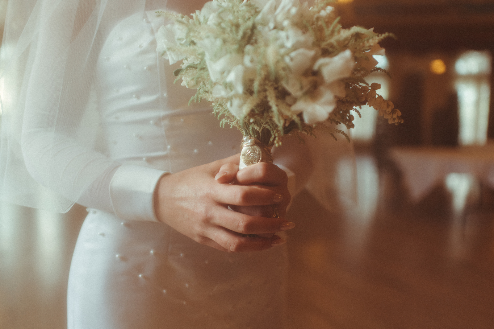 Tyller's hands clasped around the stem of her bouquet, showing the family charm secured at the top of the stem wrap underneath the flowers.