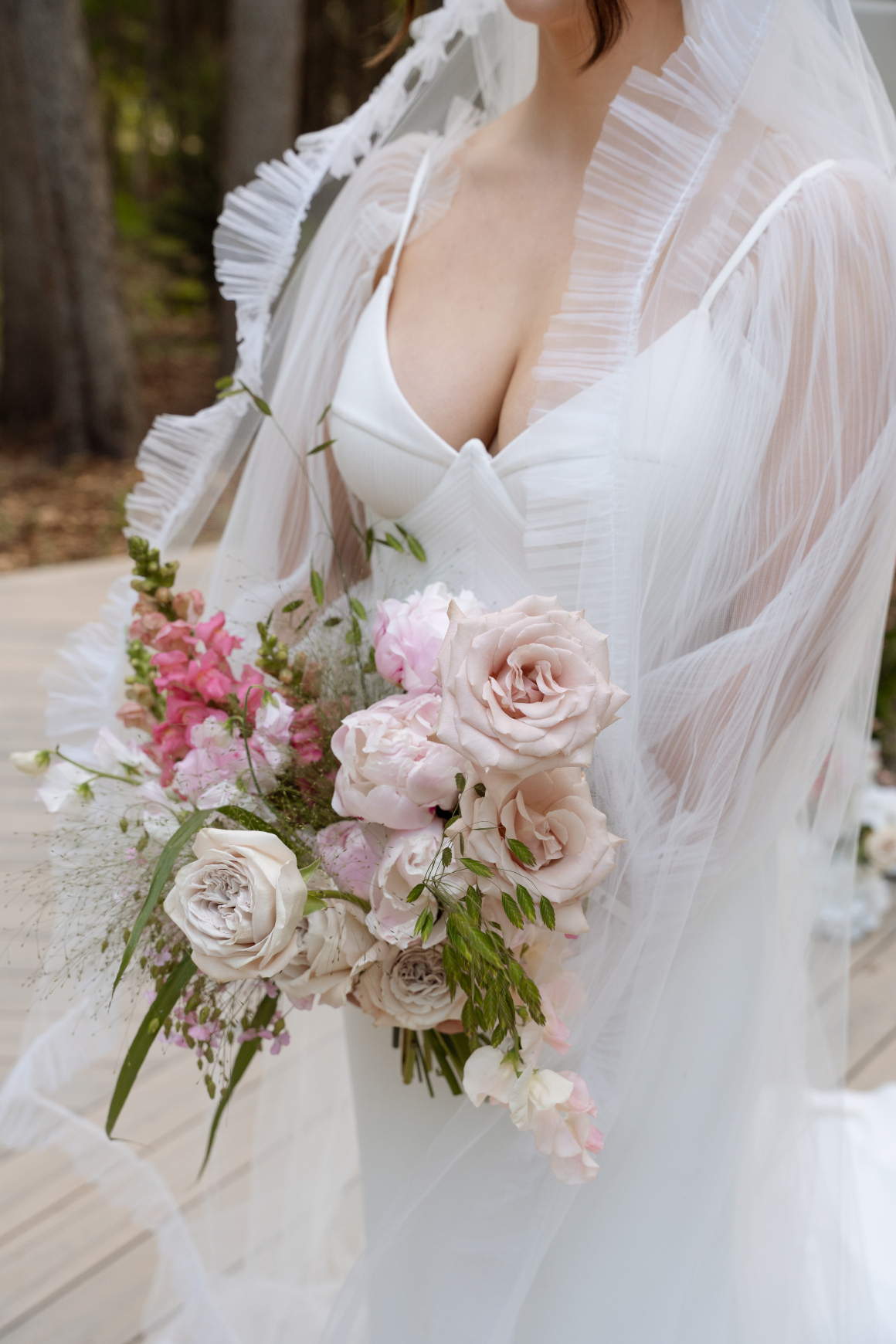 A photo of the bride from the neck down, showing her beautiful veil with a delicate ruffled edge, gorgeous gown and gorgeous bouquet.