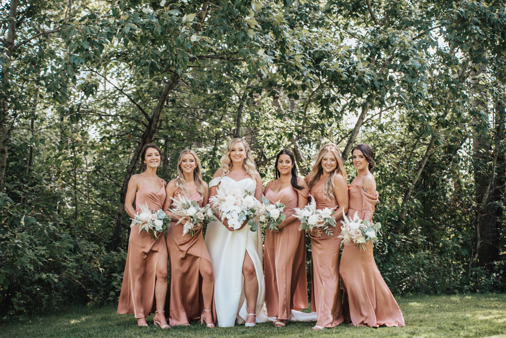Holly is standing with her bridesmaids in Sienna coloured gowns holding their Calyx Floral Design bouquets of roses, orchids, pampas grass, dried fern and eucalyptus.