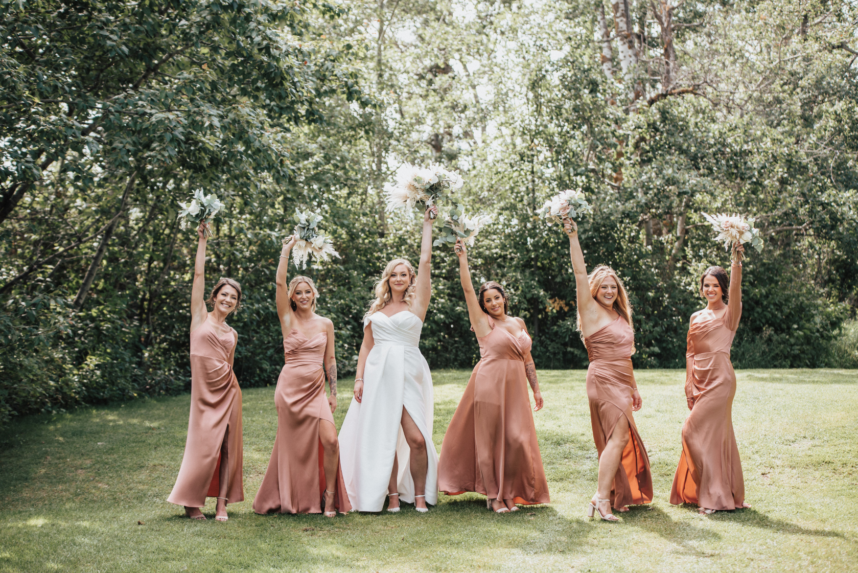 Holly and her bridesmaids strike a pose, standing with one hand in the air with their bouquet