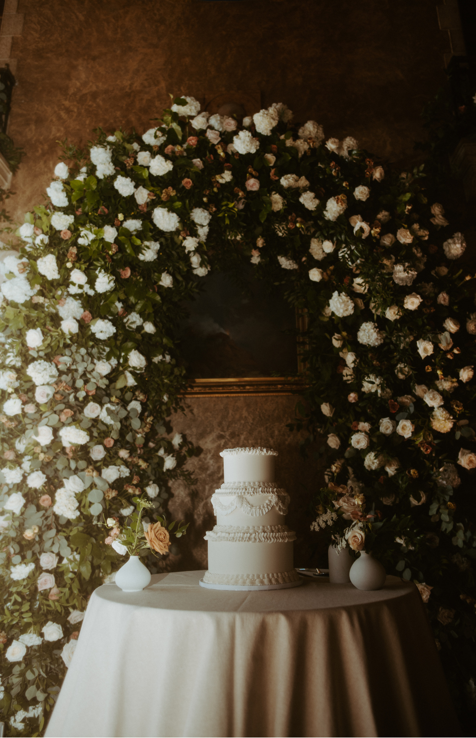Their pretty three-tiered cake in front of the fabulous, floral arch.
