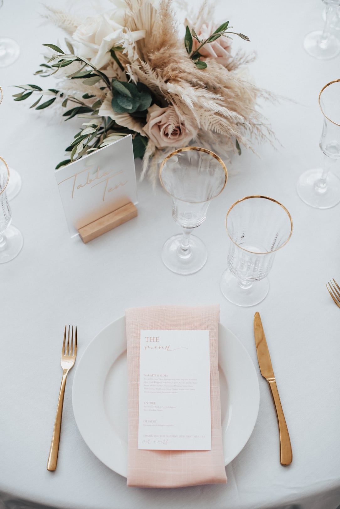 An image of a place setting at the table, with the perfectly coordinated details, pretty frosted glass table numbers and floral centrepiece.